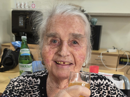 Eine lächelnde ältere Frau hält ein Glas mit einem Getränk in der Hand.