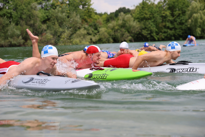 Mehrere Sportler paddeln mit Rettungsboards im Wasser.
