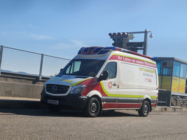 Rettungswagen mit blauem Licht, Parkposition, Logo und Kontaktinformationen sichtbar.