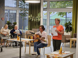 Eine Frau singt und spielt Gitarre, während andere zuhören.