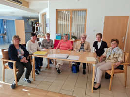 Gruppentreffen von sieben Frauen an einem Tisch in einem hellen Raum.