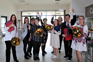 Gruppensieger feiern mit Blumensträußen und Daumen hoch in einem modernen Raum.