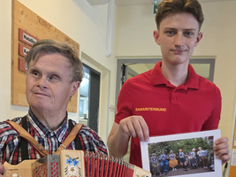 Zwei Männer, einer mit einem Akkordeon, der andere mit einem Dankesbrief.