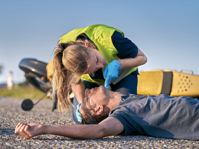Eine Person leistet Erste Hilfe an einem verletzten Mann auf dem Boden.