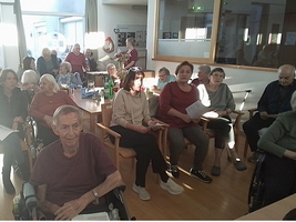 Eine Gruppe älterer Menschen sitzt in einem Raum, einige mit Notizen in der Hand.