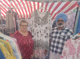 Zwei Personen stehen auf einem Markt und präsentieren Kleider.