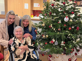 Drei Frauen stehen zusammen vor einem festlich geschmückten Weihnachtsbaum.