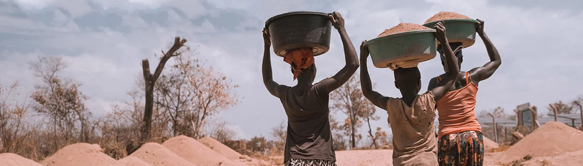 Drei Afrikanerinnen tragen Plastikbehälter, gefüllt mit Erde, auf dem Kopf