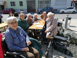 Ältere Personen sitzen an einem Tisch im Freien und genießen Getränke.