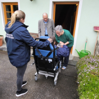 Eine Betreuerin interagiert mit einem älteren Paar vor einem Haus.