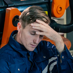 Ein erschöpfter Arbeiter sitzt neben einem industriellen Roboter.
