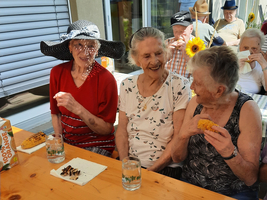 Drei ältere Frauen sitzen zusammen und genießen Essen und Getränke.