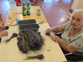 Zwei ältere Frauen binden Lavendelsträuße am Tisch.