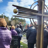 Menschen versammelt an einem Grabstein während einer Trauerfeier im Freien.