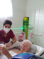 Pflegekraft und ältere Frau stoßen mit Gläsern im Bad an.