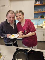 Zwei Personen lächeln in einer Küche und halten einen Teller mit einem Ei.