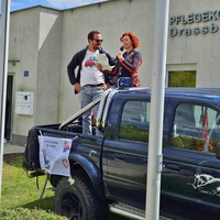 Zwei Menschen stehen auf einem Pickup und sprechen vor einem Gebäude.