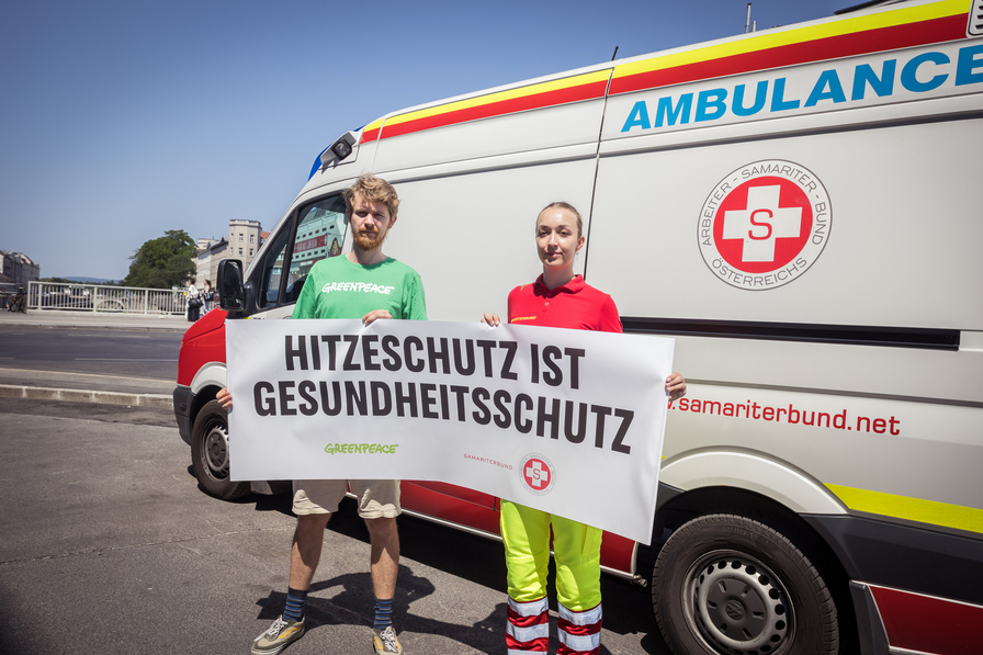 Zwei Personen stehen vor einem Krankenwagen. Sie halten ein großes Banner mit der Aufschrift 