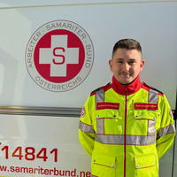 Ein Sanitäter in Uniform steht vor einem Rettungsauto des Samariterbundes.