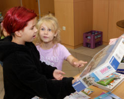 zwei Kinder, ein Kind im Vordergrund nimmt ein Puzzle entgegen, anderes Kind dahinter zeigt darauf 
