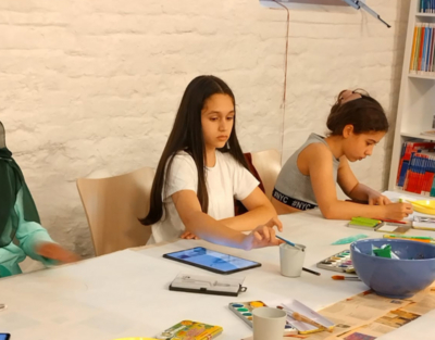 Zwei Mädchen sitzen am Tisch mit Pinseln in der Hand und malen 