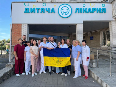 Gruppe von Ärzten und Mitarbeitern hält eine ukrainische Flagge vor einem Krankenhaus.