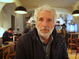 Mann mit grauen Haaren und Bart, sitzt in einem gemütlichen Café.