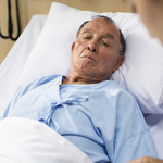 Ein älterer Mann liegt im Krankenhausbett, während eine Krankenschwester sich um ihn kümmert.