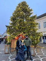 Familie steht vor einem festlich geschmückten Weihnachtsbaum auf einem Platz.