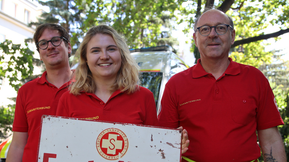 3 Samariter:innen mit Vintage-Hinweisschild