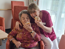 Seniorin und Pflegerin essen einen Faschingskrapfen.