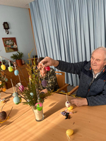 Zwei Senioren dekorieren einen Osterbaum mit bunten Eiern.