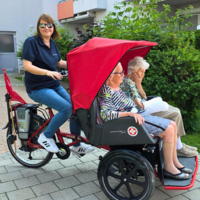 Eine Frau fährt mit einem Lastenrad zwei ältere Damen spazieren.