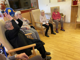 Ältere Frauen sitzen zusammen, eine hebt einen bunten Ball in der Hand.