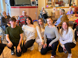 Junge Menschen posieren lächelnd vor Senior*innen im Aufenthaltsraum.