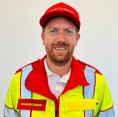 Ein lächelnder Mann in einer gelb-roten Uniform des Samariterbundes.