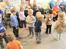Kinder tanzen und singen, während eine Frau mit Gitarre spielt.
