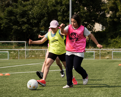 zwei Mädchen beim Fußballspielen laufen auf Ball zu, links mit gelbem Trikot, rechts mit rosa Trikot