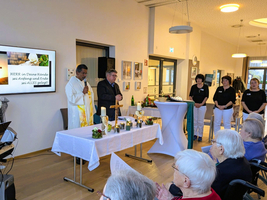 Eine religiöse Zeremonie mit einem Priester und Teilnehmern in einem Gemeinschaftsraum.
