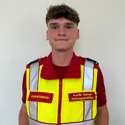 Junger Mann in Rettungsdienstuniform mit Namen und Verbandsschildern.