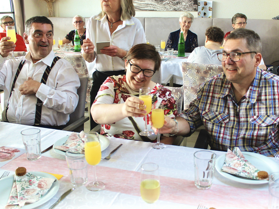 Eine Gruppe von Menschen erhebt Gläser beim Anstoßen an einem gedeckten Tisch.
