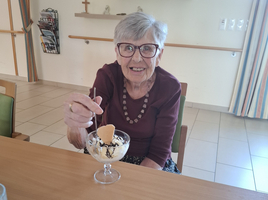 Ältere Frau lächelt mit einem Eisbecher in der Hand.