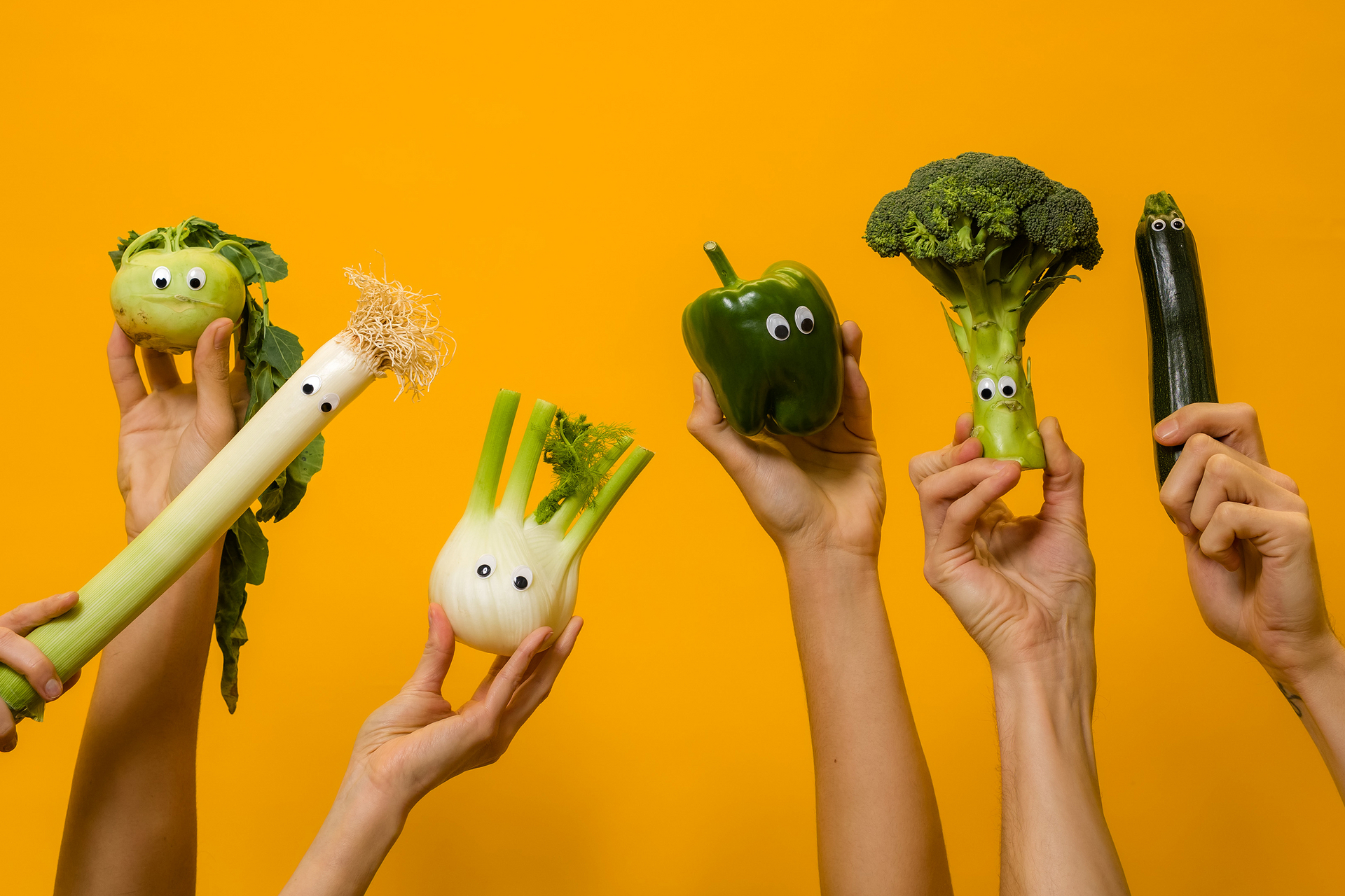 Sechs Hände halten je ein Stück Gemüse mit aufgeklebten Augen