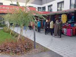 Marktstand mit verschiedenen Kleidungsstücken und einer Kundin mit Rollator.