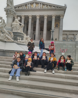 Eine Gruppe Mädchen sitzt vor dem Parlament in Wien und lächelt in die Kamera.
