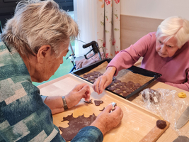 Zwei ältere Personen backen gemeinsam Plätzchen in einer hellen Küche.