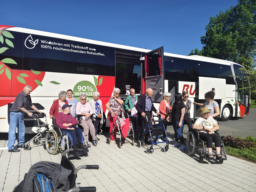 Ältere Menschen steigen aus einem Bus und sammeln sich im Freien.
