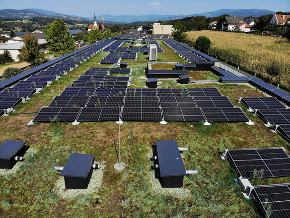 Die Photovoltaikanlage am Dach des Pflegekompetenzzentrums von oben aufgenommen. Sie besteht aus mehreren Solarmodulen. Die Module sind in Reihen angeordnet, umgeben von Gras und anderen Elementen.