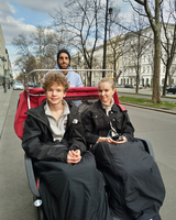 Drei Personen sitzen in einem Rollstuhl auf einer Straßenfahrt.