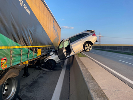 Ein Auto hängt gefährlich am Rand eines Lkw auf der Autobahn.